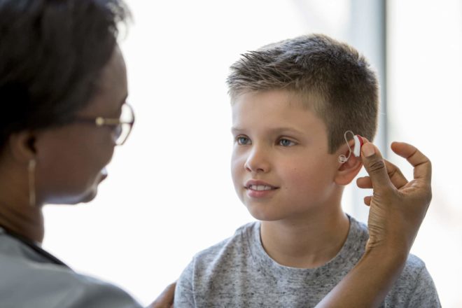 An audiologist adjusting a hearing aid on a young boy at Estes Audiology in New Braunfels, TX.