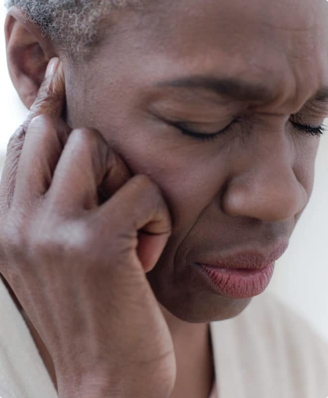 African American woman holding her ear in pain from tinnitus