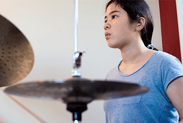 A female musician with hearing aids plays a drum set in Michigan.